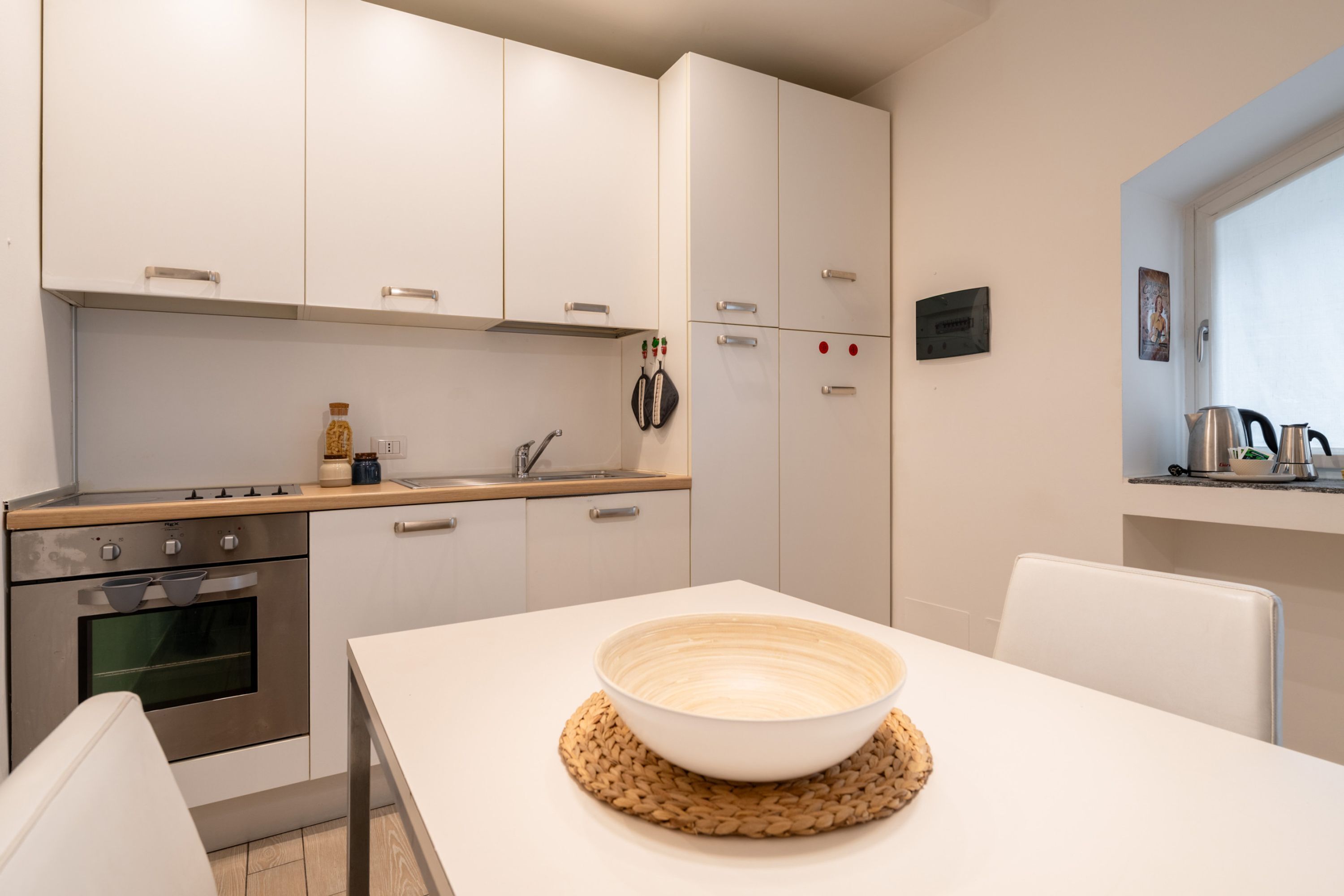 Et moderne køkken med hvide skabe, en ovn i rustfrit stål og et spisebord med en skål.