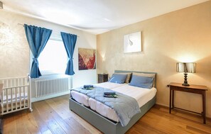 A bedroom with a bed, a nightstand, a lamp, a radiator, and a crib.