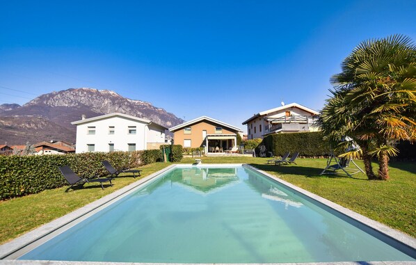 A swimming pool with lounge chairs, a mountain backdrop, and a building with a balcony.