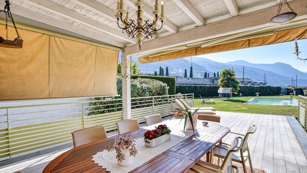 An outdoor patio with a wooden table and chairs, a pool, and a view of mountains.