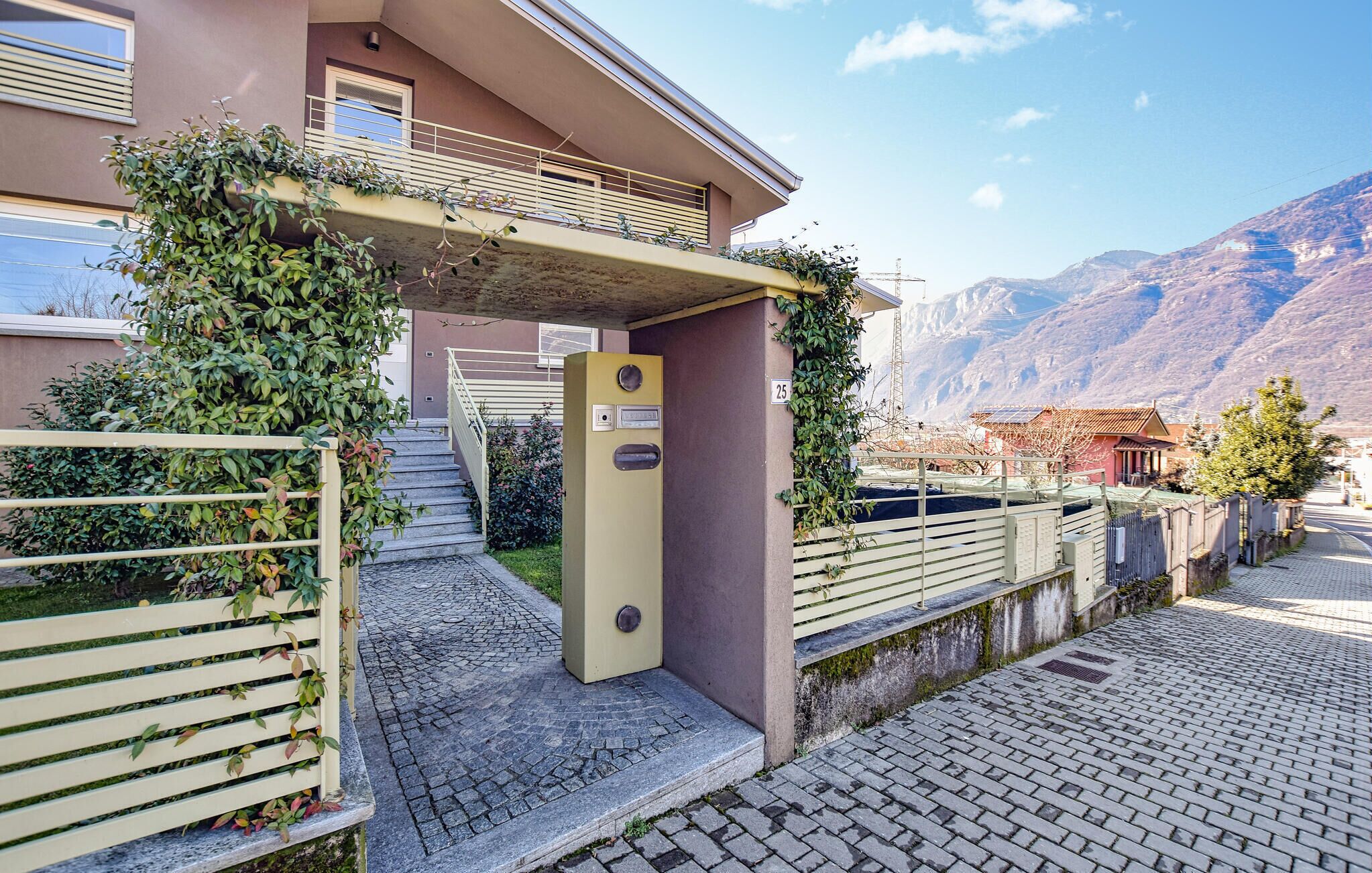 A building with a staircase leading to a balcony, a gate, and a mountainous backdrop.