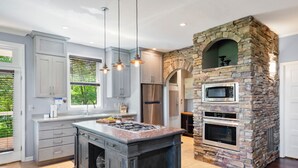 A modern kitchen with a central island, built-in appliances, and a stone accent wall. - Point of View (Fairview)