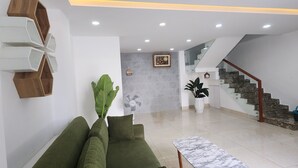 Una sala de estar moderna con un sofá verde, una mesa de centro de mármol, un piano y una escalera que conduce a un nivel superior.