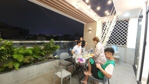 Un área de comedor en la azotea con una mesa preparada para cuatro personas, rodeada de plantas en macetas e iluminación moderna.