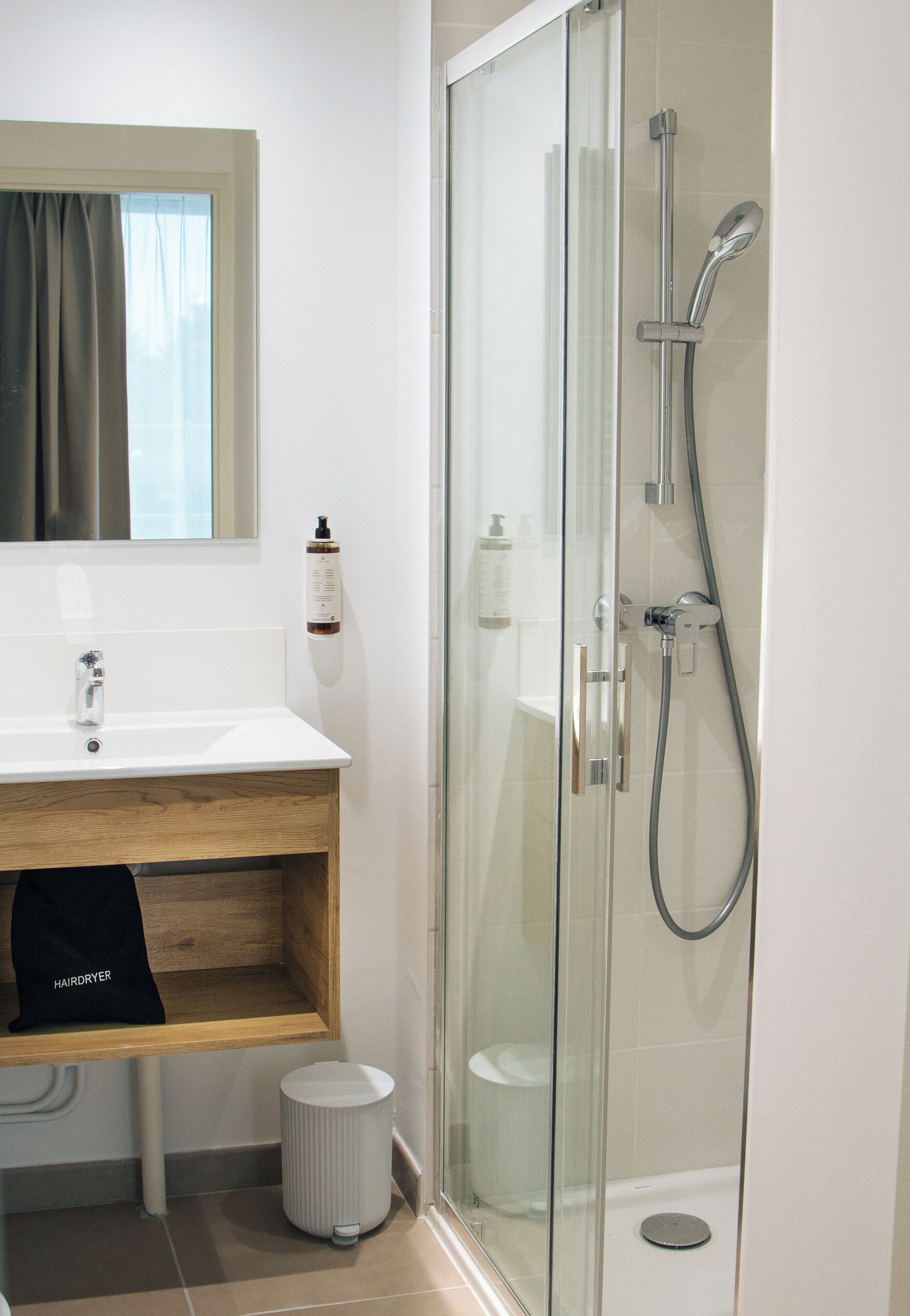 A bathroom with a glass-enclosed shower, a wooden vanity, a mirror, and a hairdryer bag.