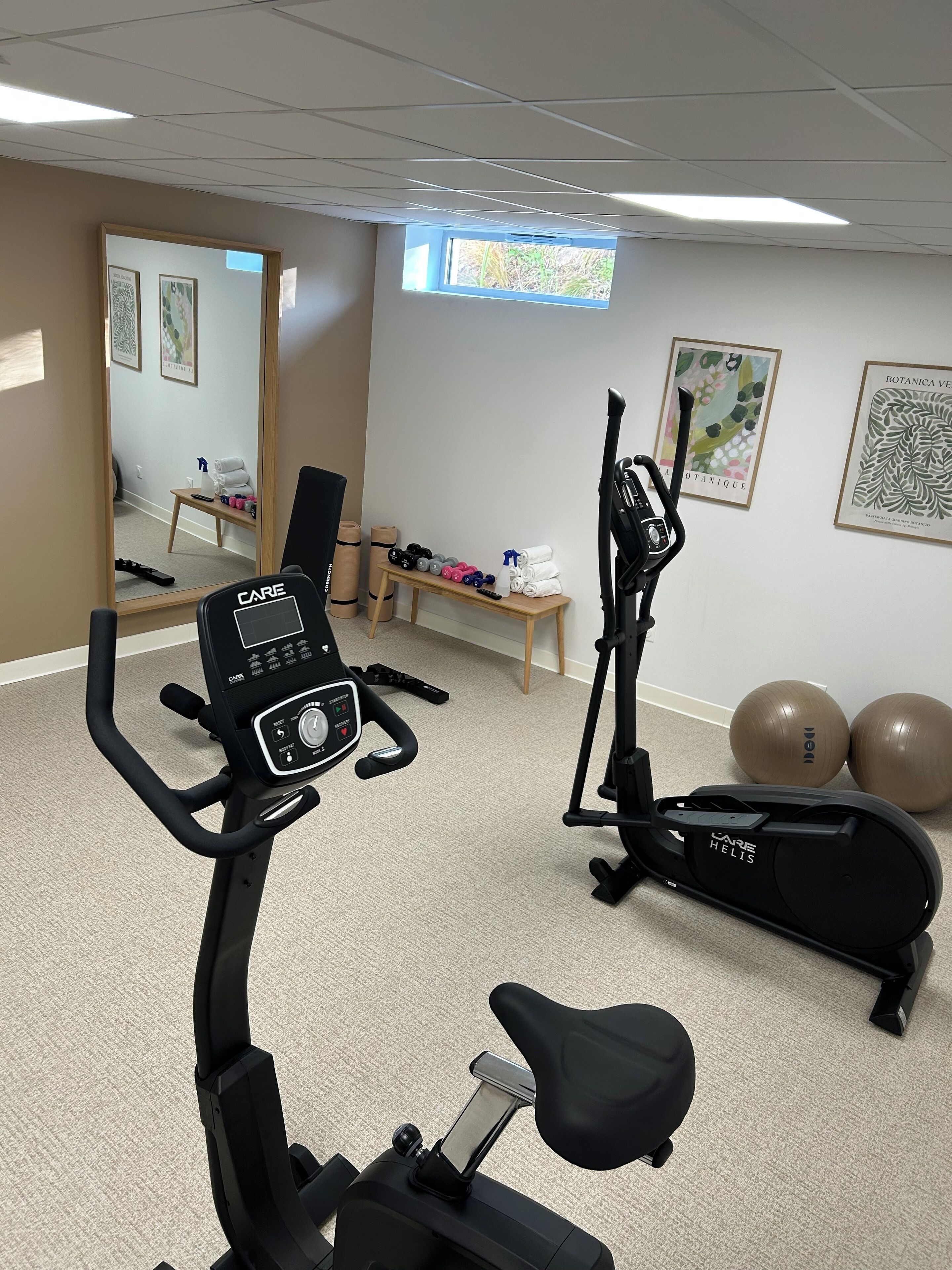 Une salle de remise en forme équipée de matériel d’exercice, d’un miroir, d’une petite table avec des serviettes et de ballons d’exercice.