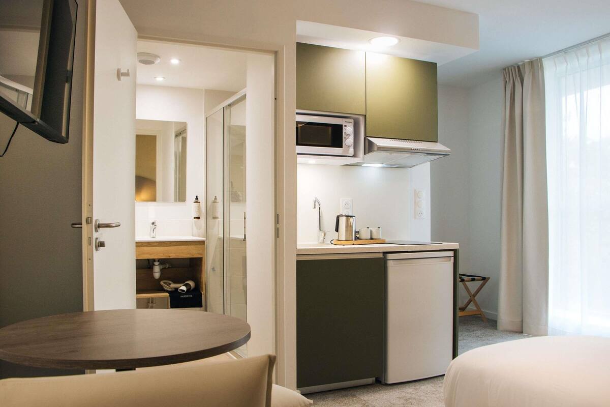 A compact hotel room with a kitchenette, a small dining table, and a bed.