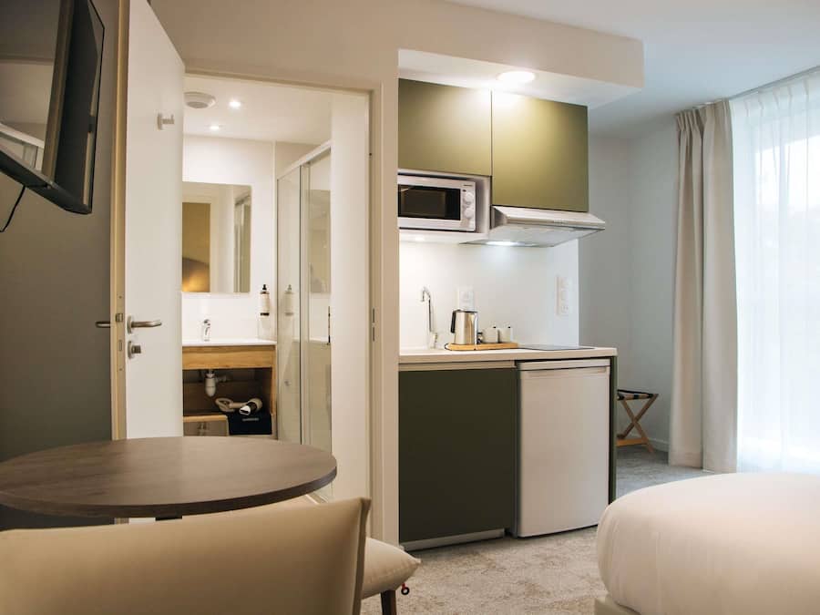 A compact hotel room with a kitchenette, a small dining table, and a bed.