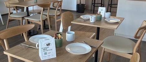 A dining area with wooden tables and chairs, a menu on the table, and a potted plant.