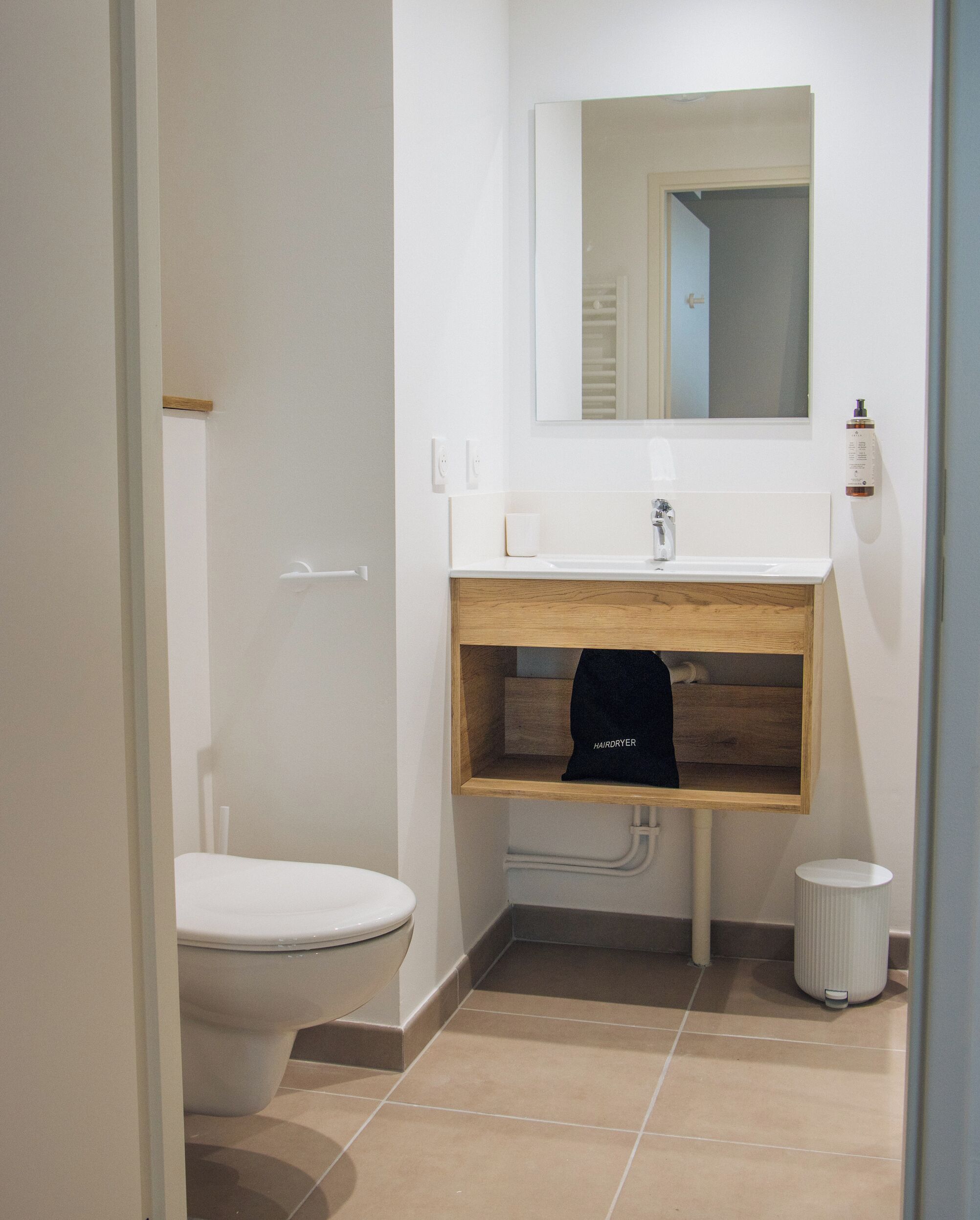 Een badkamer met een toilet, een wastafel met spiegel erboven en een handdoek aan een houten plank.