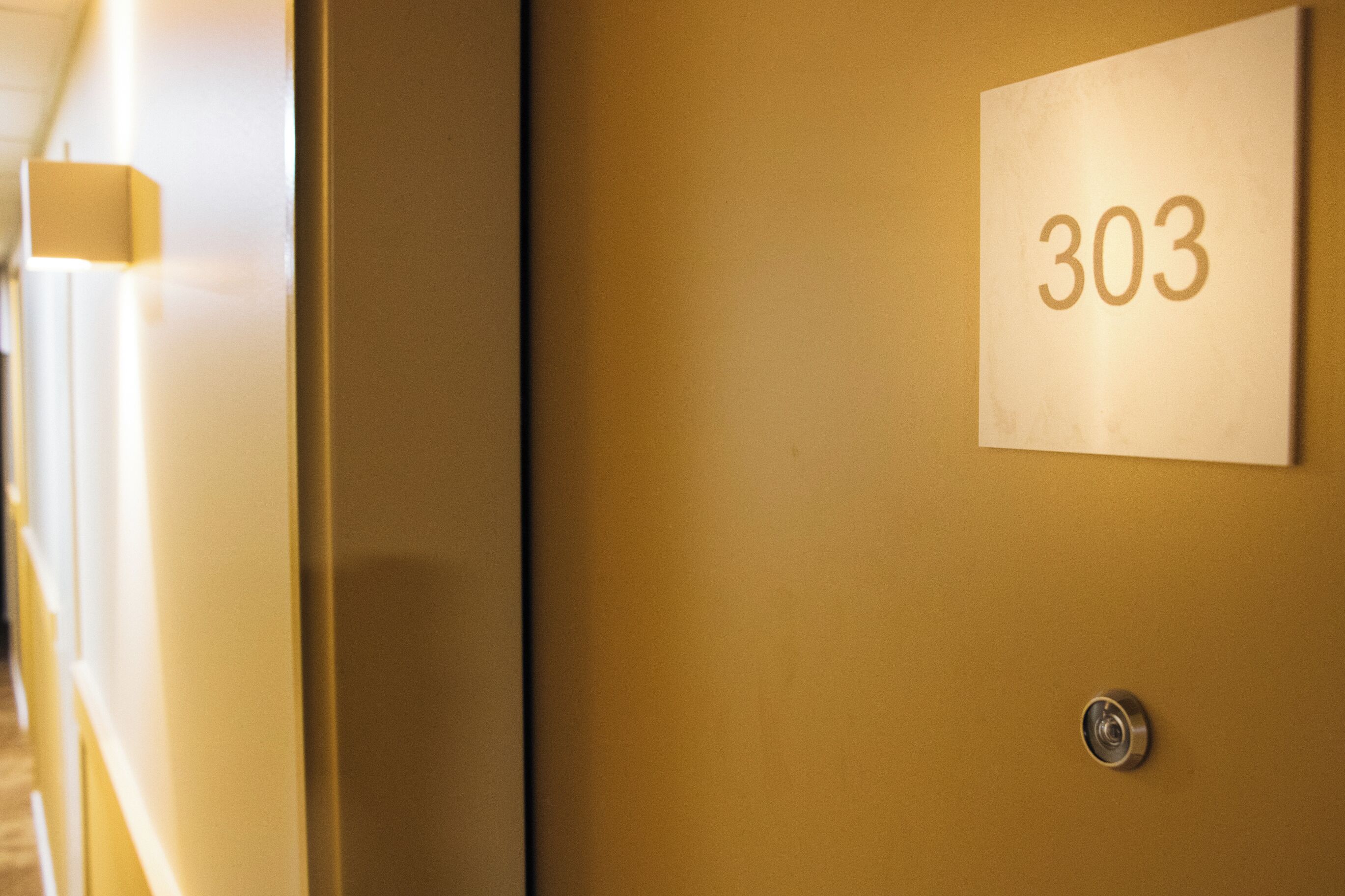 A close-up of a room number sign '303' on a wall, a door handle, and a light fixture.