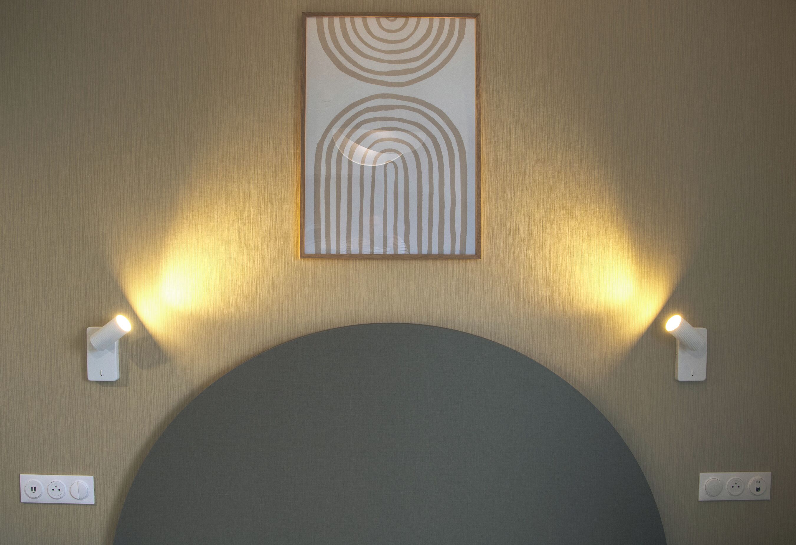 Eine Wand mit einem großen, runden Objekt, zwei Wandleuchten und einem gerahmten Kunstwerk darüber.