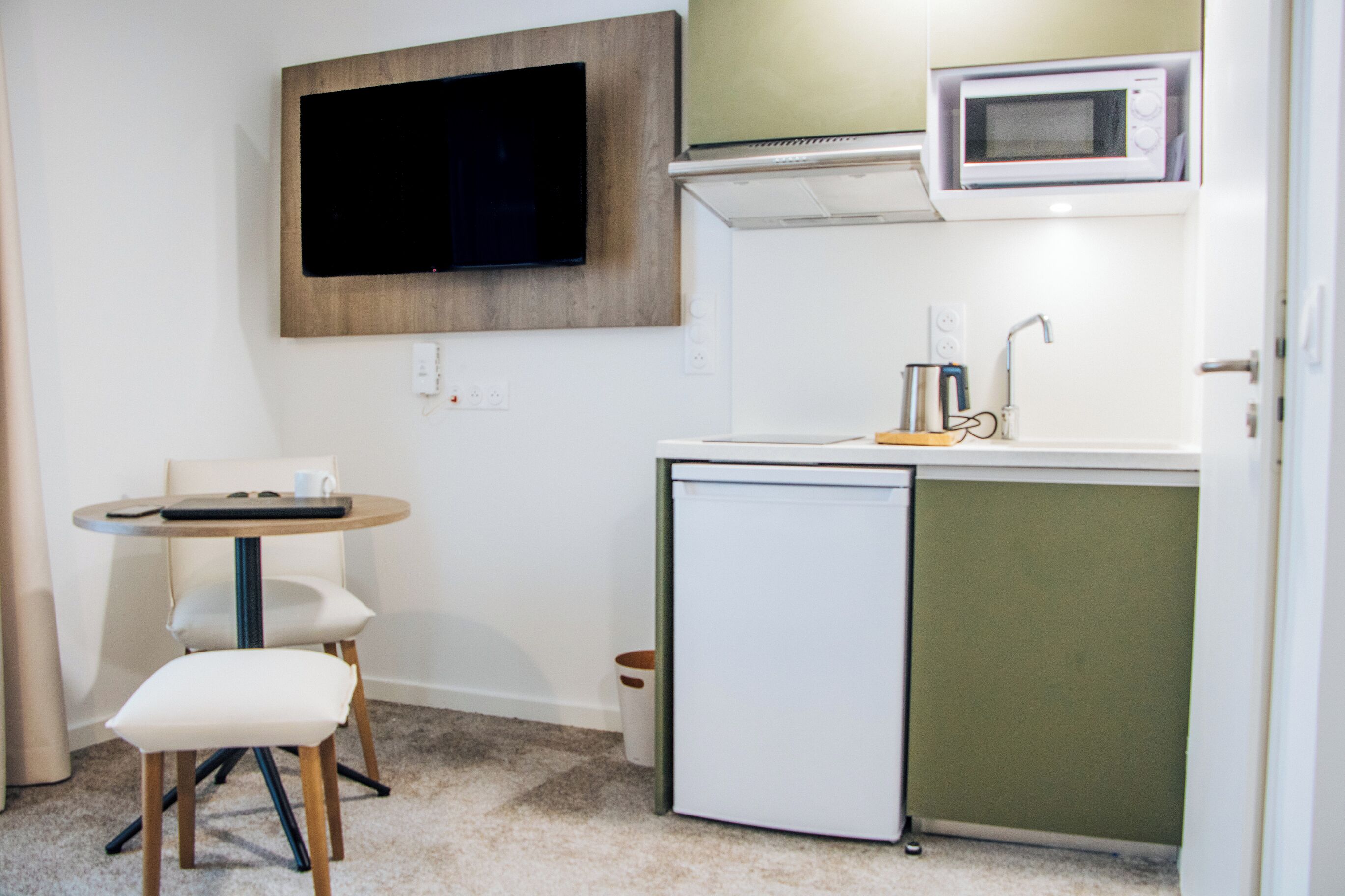 A compact kitchenette with a microwave, a small sink, and a flat-screen TV mounted on the wall.