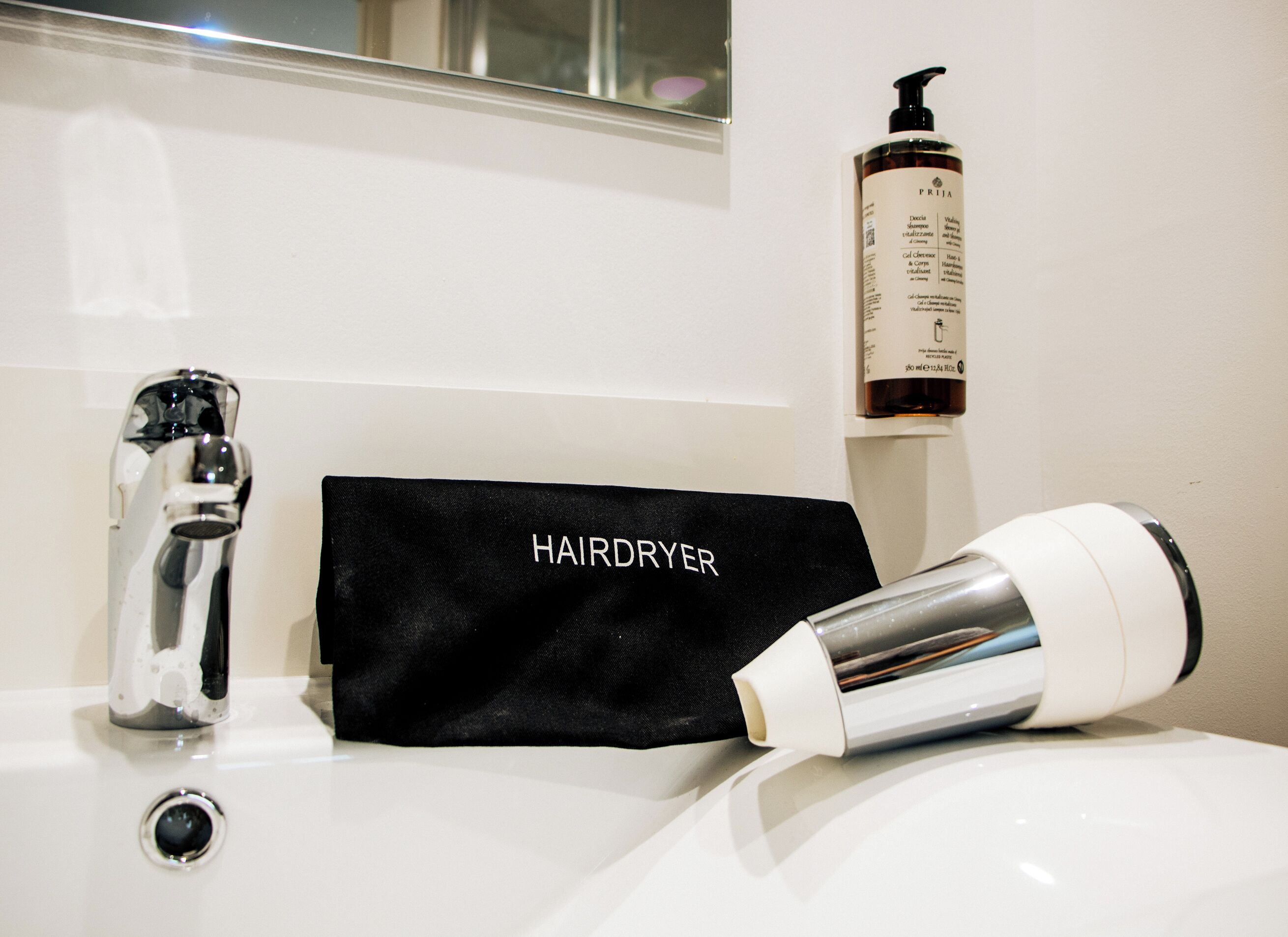 A bathroom sink with a hairdryer, a black hairdryer bag, and a bottle of hair care product.