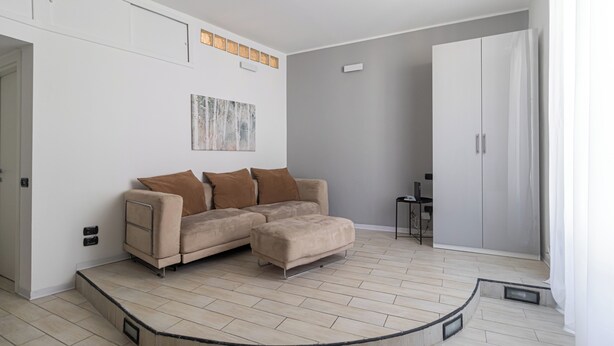 A modern living room with a beige sectional sofa, a small table with a laptop, and a grey accent wall. - Italianway Easy - Ticinese 83, 15 min to Linate (Milan)