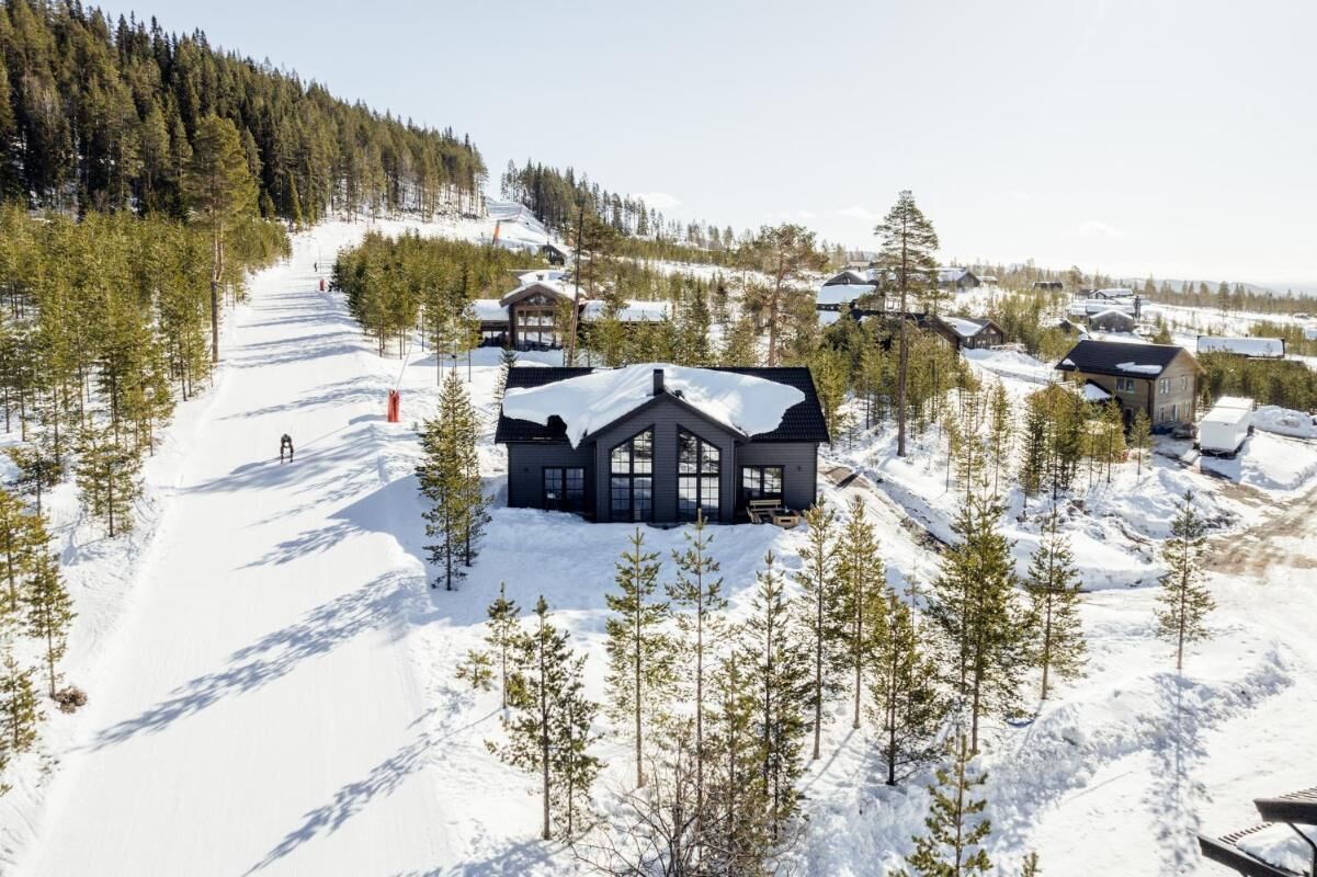 Una cabaña nevada con un edificio central grande, rodeada de pequeñas cabañas y árboles.