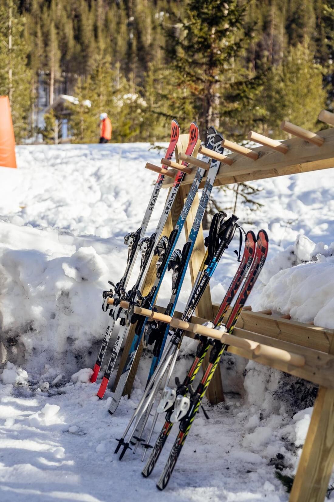 A wooden ski rack with multiple skis and ski poles.