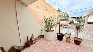 Een balkon met potplanten, een witte muur en uitzicht op de straat.