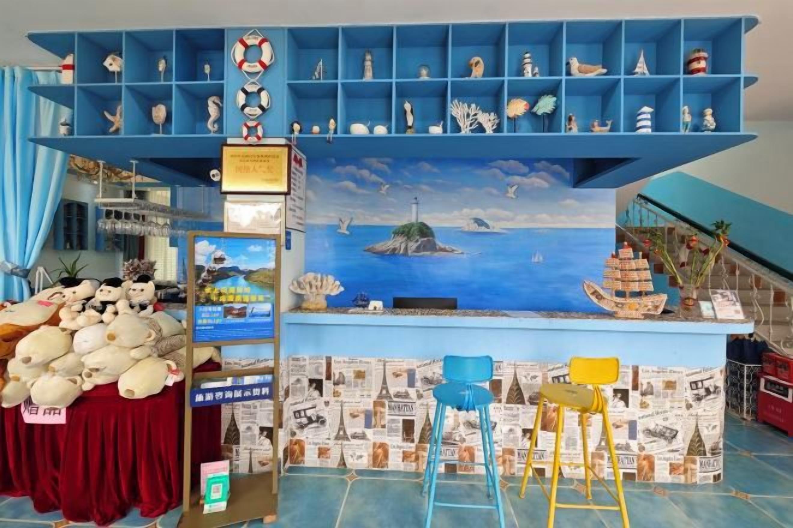 A room with a blue wall, a shelf with various items, a table with stuffed animals, and a mural of a sea scene.