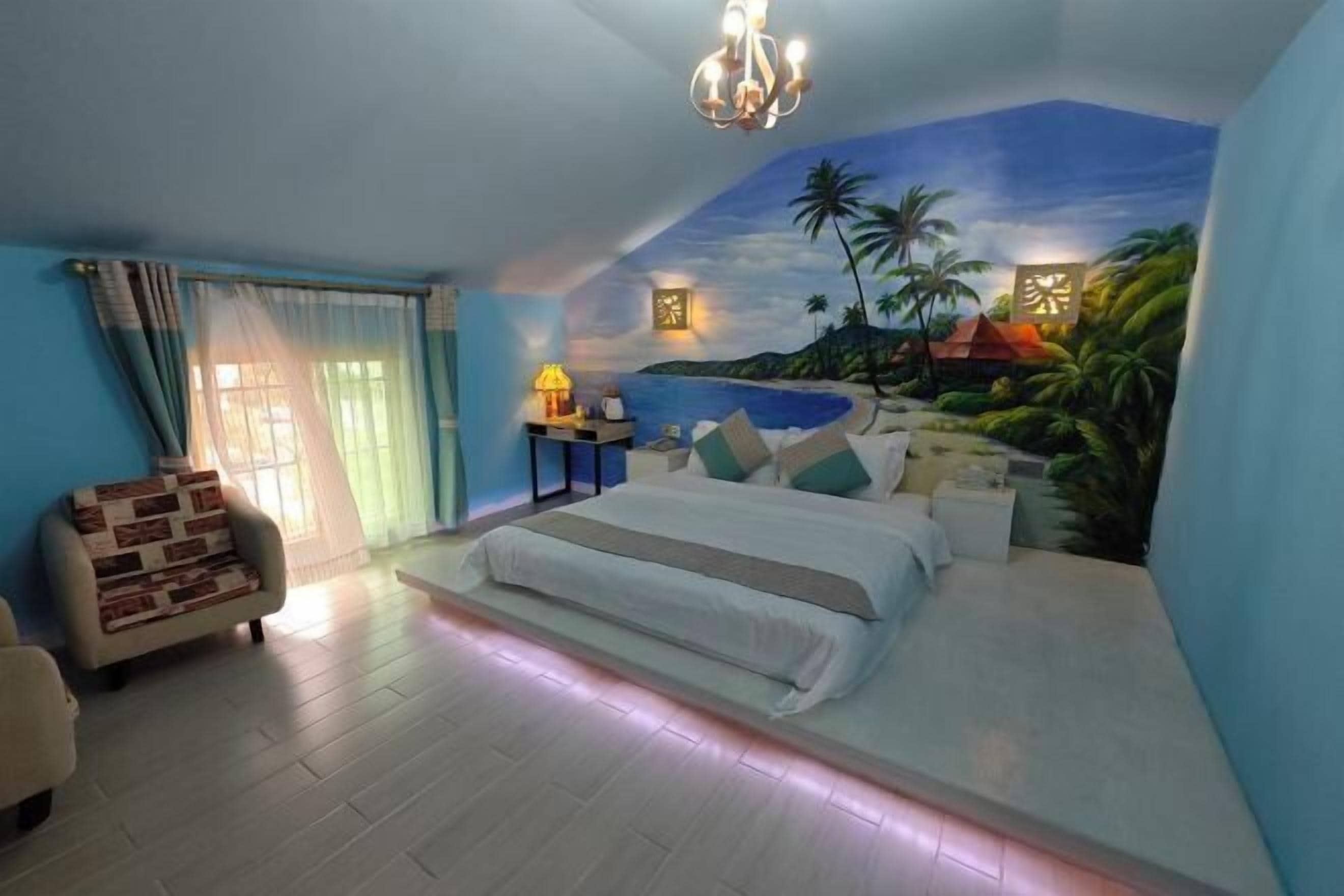 A bedroom with a bed, a chair, a nightstand, and a mural of a tropical beach scene.