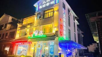 Un edificio de varios pisos con señalización iluminada, un restaurante en la planta baja y mesas al aire libre.