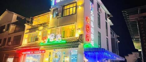 A multi-story building with illuminated signage, a restaurant on the ground floor, and outdoor seating.