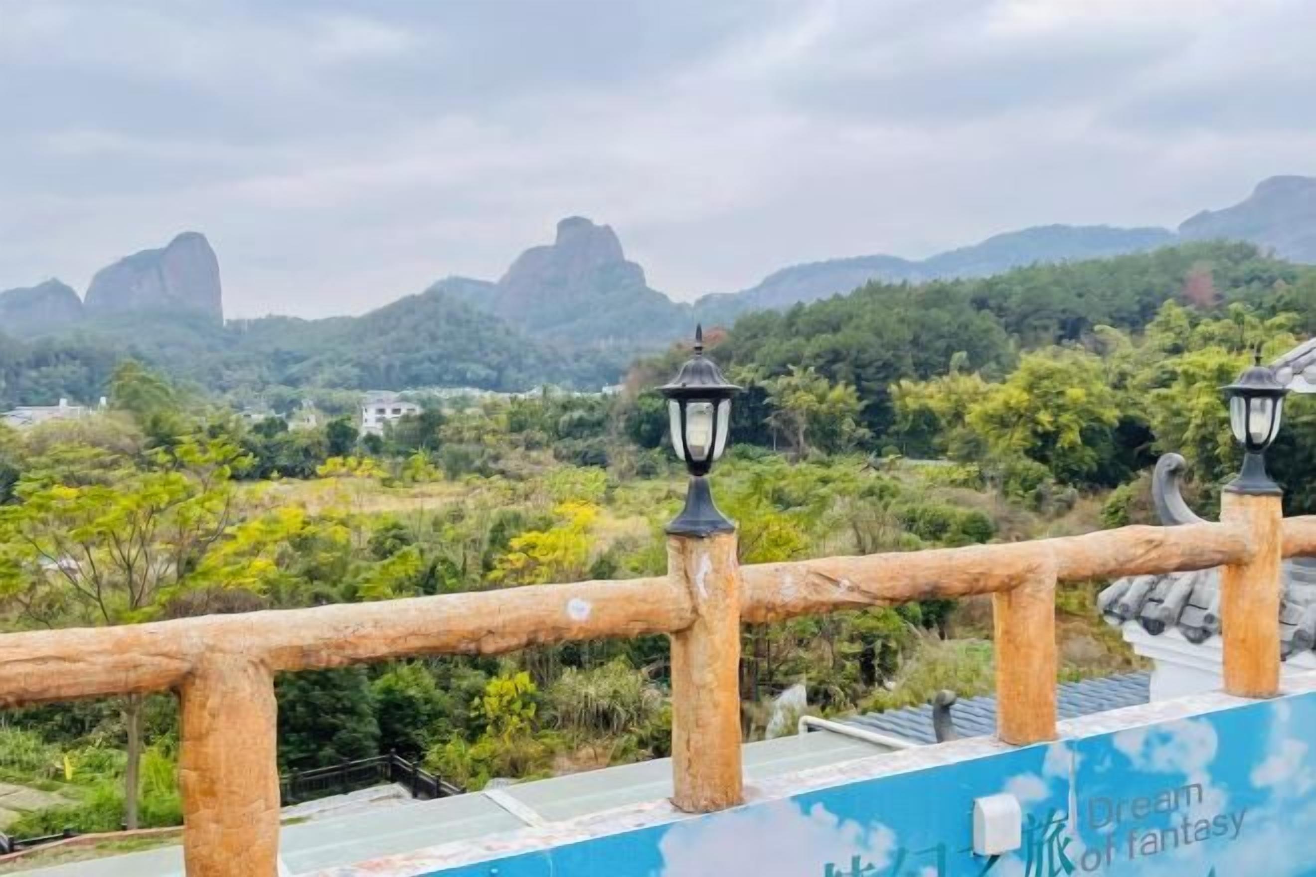 A view from a balcony with a railing, overlooking a landscape with trees and distant mountains.