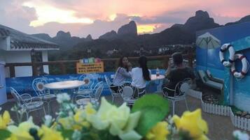 An outdoor seating area with tables and chairs, overlooking a mountainous landscape.