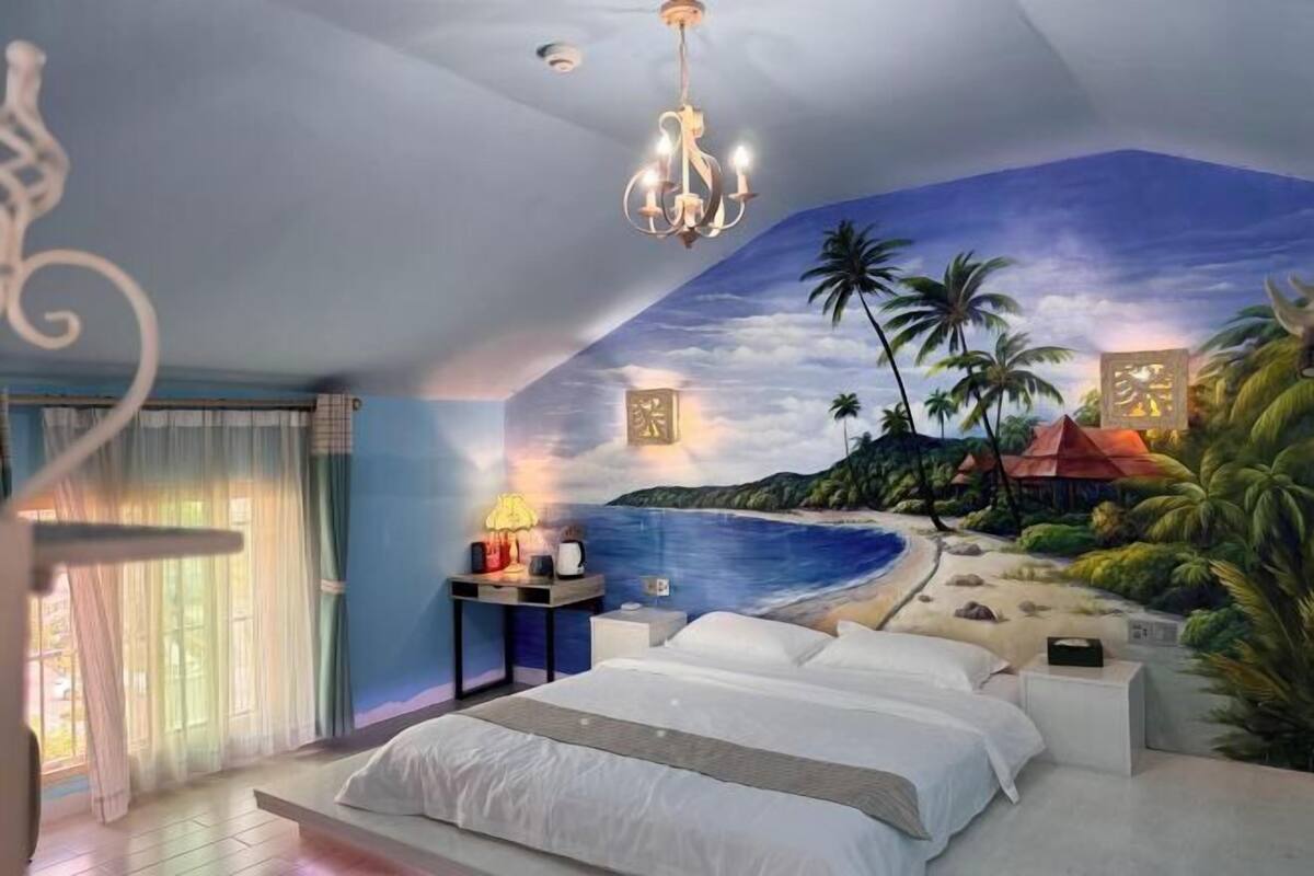 A bedroom with a mural of a beach scene, a bed, bedside tables, and a chandelier.