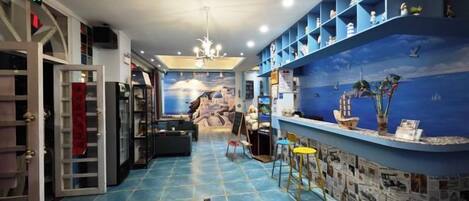 A room with a blue tiled floor, a chandelier, a bar area with a ship mural, and shelves with decorative items.