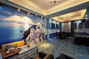 Una habitación con un mural de paisaje costero, un comedor con mesa y sillas, y una araña.