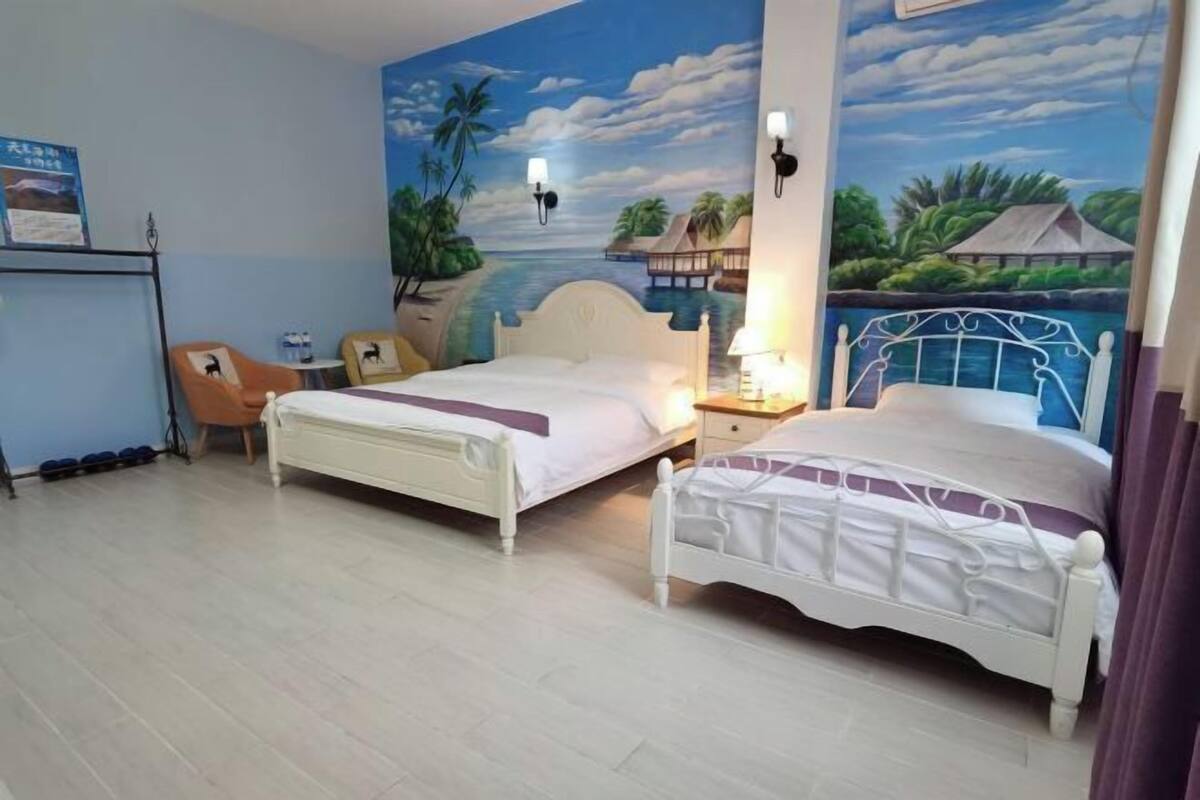 A hotel room with two beds, a desk, a chair, and a mural of a tropical scene.