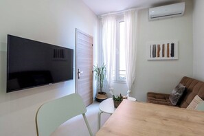 Un salon équipé d’un téléviseur à écran plat, d’une table à manger, d’un canapé et d’une plante en pot.
