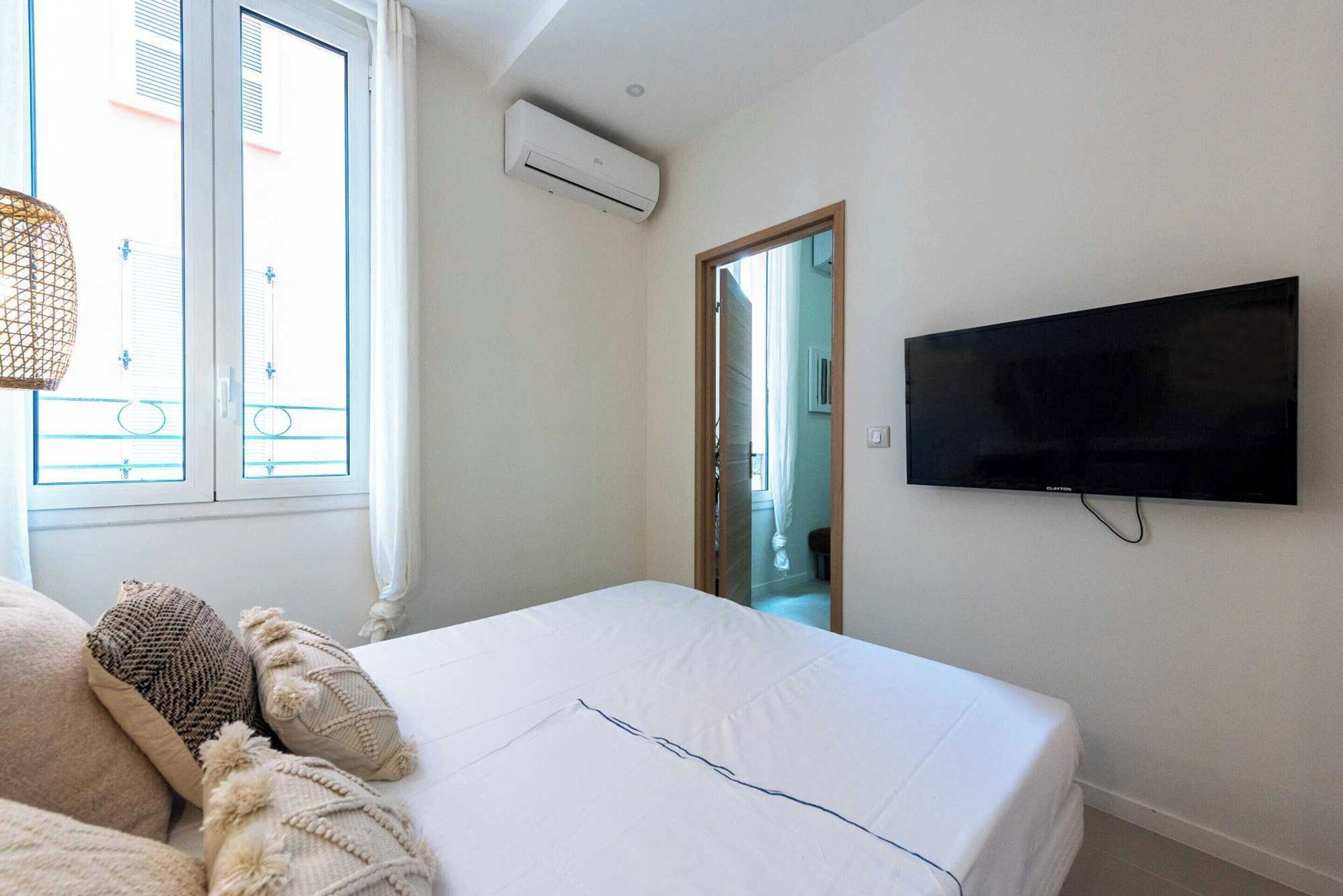 A bedroom with a bed, a TV mounted on the wall, and an air conditioning unit.