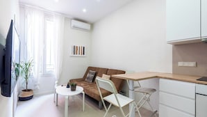 Un espace de vie compact comprenant un coin cuisine, un canapé, une table à manger et une plante en pot.