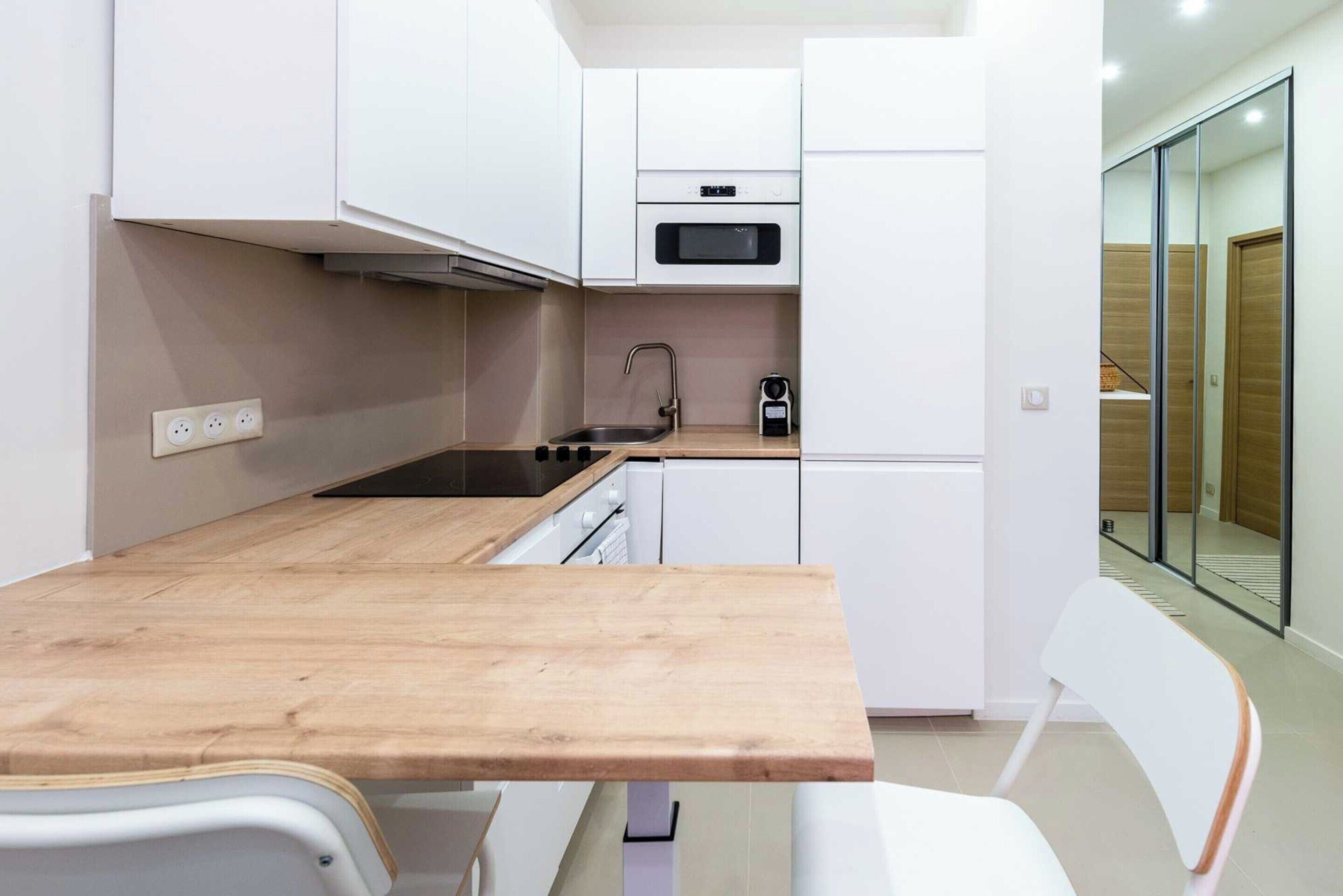 Een kleine keuken met witte kastjes, een houten aanrechtblad, een inbouwoven en een koffiezetapparaat.