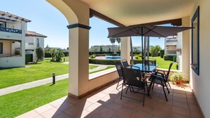 A covered patio with a table and chairs, overlooking a swimming pool and well-maintained garden. - San Bruno - Playa Isla Canela ISHBII13P13 (Isla Canela)