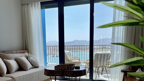 A modern living room with a sofa, a coffee table, and a view of a pool and mountains. - Aladdin Chalets - 2.5 Bedrooms (Aqaba)