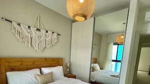A bedroom with a large bed, a macrame wall hanging, a woven light fixture, and a mirror reflecting the room. - Aladdin Chalets - 2.5 Bedrooms (Aqaba)