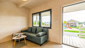 A room with a grey sofa, a small round table, and a window with a view of a playground and houses outside. - 2 bedroom amazing home in Dziwnówek (Dziwnówek)