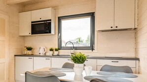 A compact kitchen with white cabinets, a black microwave, a window, and a dining table with chairs. - 2 bedroom amazing home in Dziwnówek (Dziwnówek)