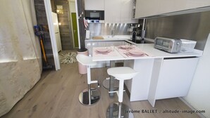 Eine kompakte Küche mit weißen Schränken, einem Edelstahlherd, einem Toaster und einer kleinen Kücheninsel mit Barhocker.