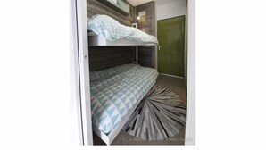 Ein Stockbett mit geometrischem Muster auf der Bettdecke, einem hölzernen Kopfteil und einer grünen Tür.