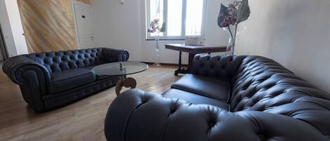 A modern living room with a black leather sofa, a glass coffee table, and a wooden floor.