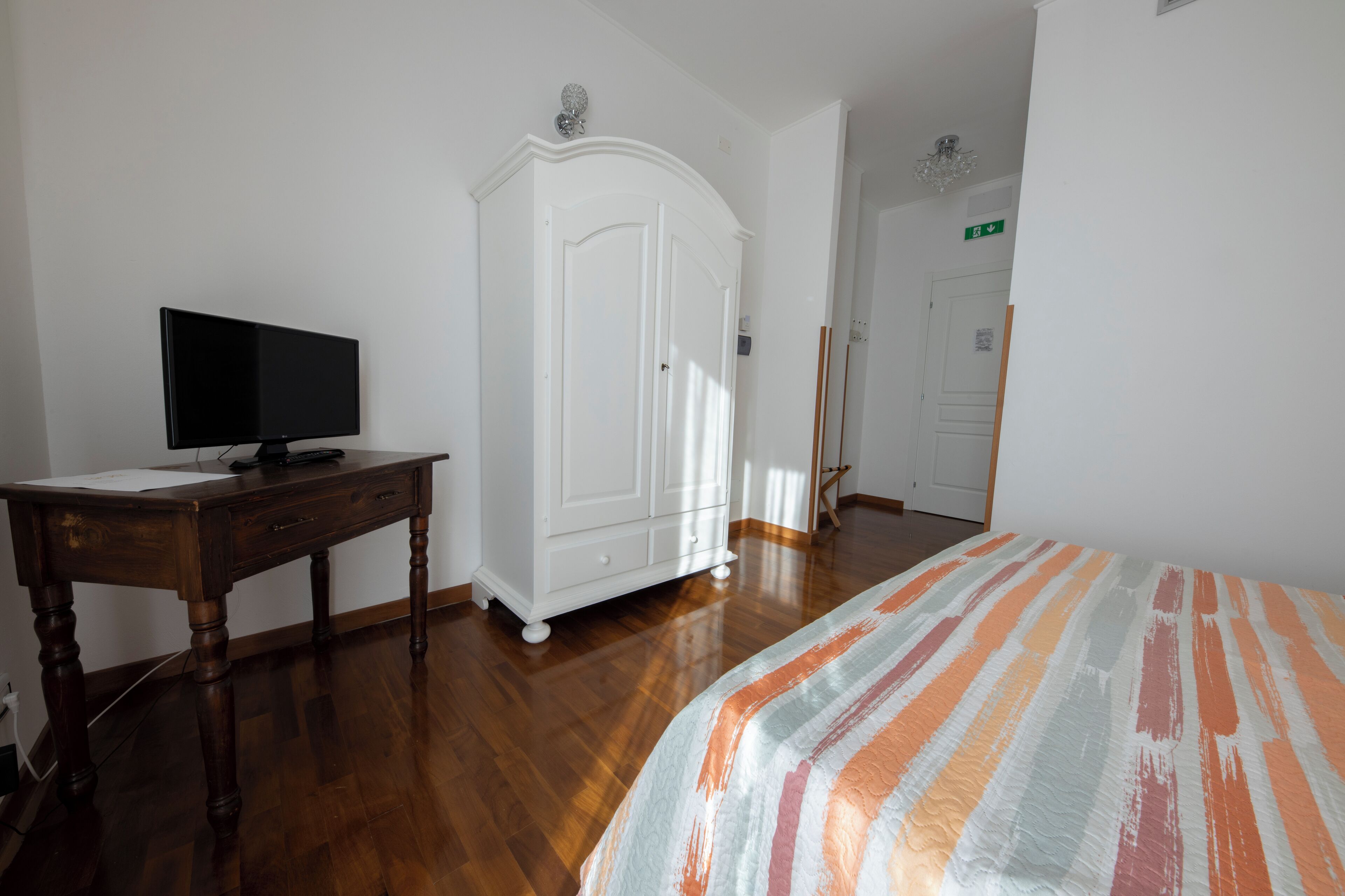 Una camera da letto con una scrivania in legno, una televisione, un armadio e un letto con lenzuola a righe.