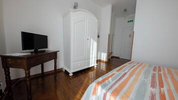 Una camera da letto con una scrivania in legno, una televisione, un armadio e un letto con lenzuola a righe.