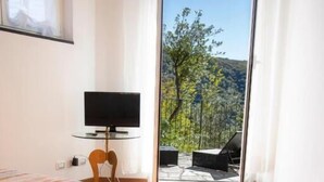 Ein Schlafzimmer mit Bett, Fernseher auf einem Nachttisch und einem Balkon mit Blick auf Bäume und Hügel.
