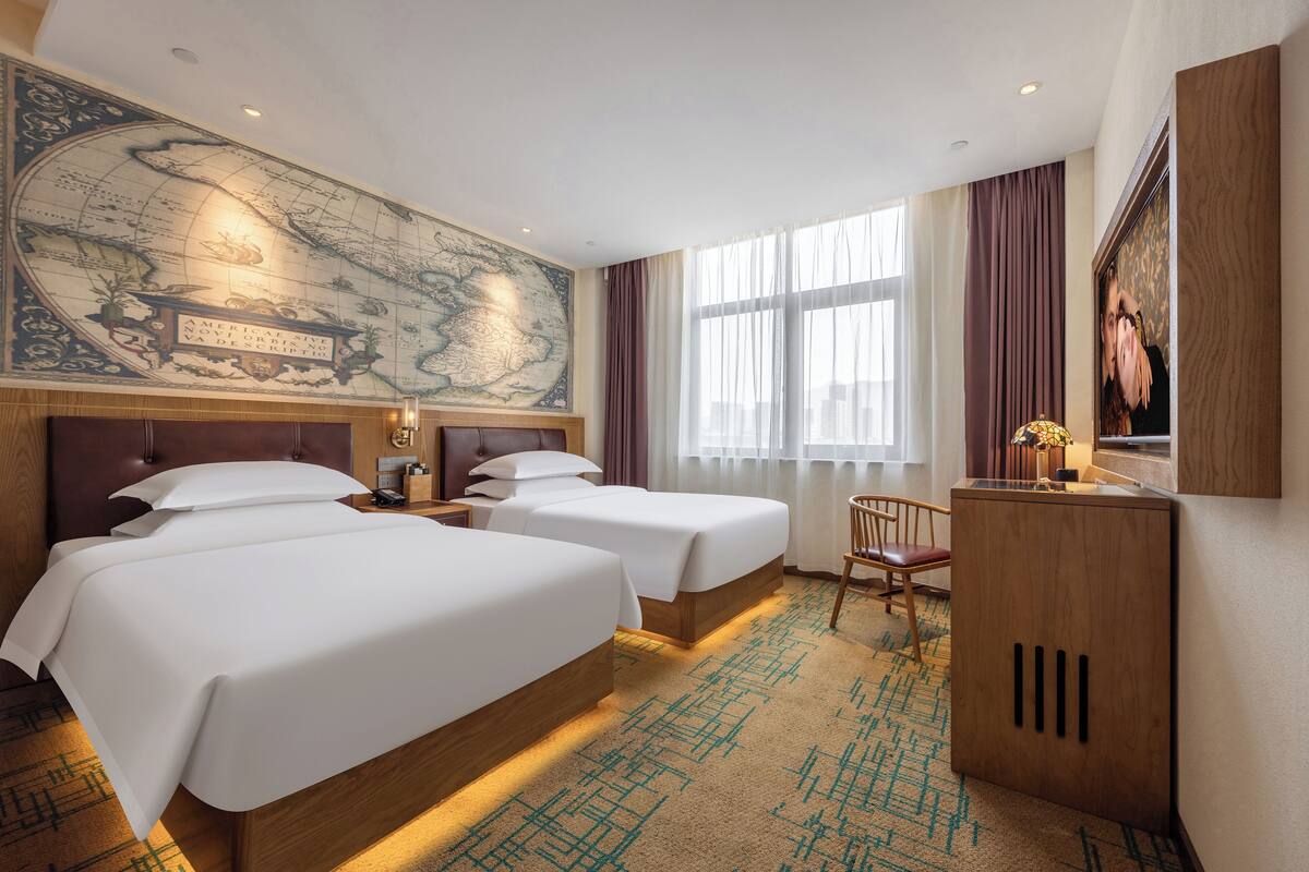 Une chambre d’hôtel avec deux lits, un bureau, une carte accrochée au mur et une grande fenêtre avec des rideaux.