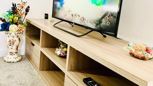 Een flatscreen televisie op een houten tv-meubel, met een bloemenvaas en kaarsen.