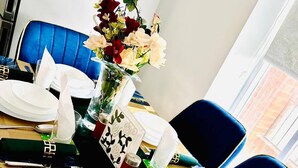 Een eettafel gedekt met witte borden, bestek en een vaas met bloemen.